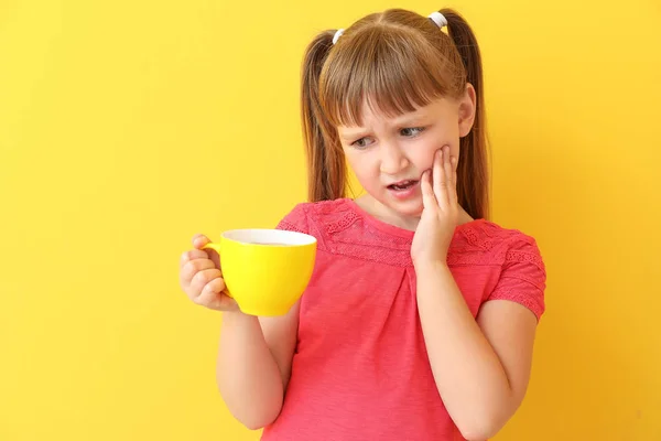 Little girl with sensitive teeth and cup of tea on color background — Stock Photo, Image