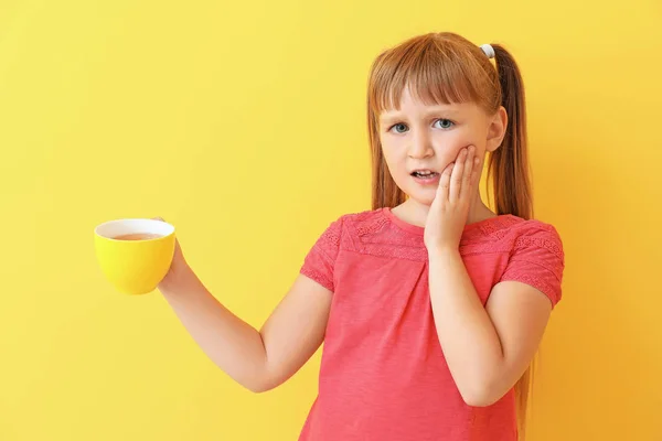 Little girl with sensitive teeth and cup of tea on color background — Stock Photo, Image