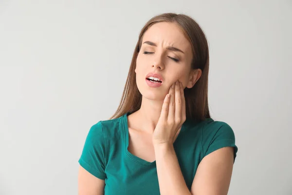 Young woman suffering from toothache against light background — Stock Photo, Image