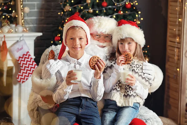 Santa Claus and little children with milk and cookies in room decorated for Christmas — Stock Photo, Image