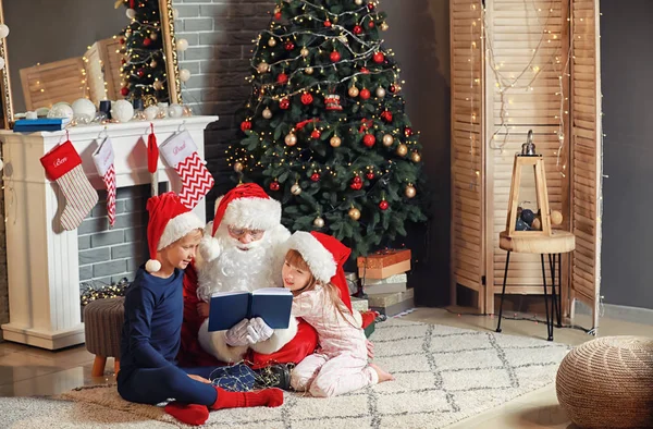 Papai Noel e crianças lendo livro no quarto decorado para o Natal — Fotografia de Stock
