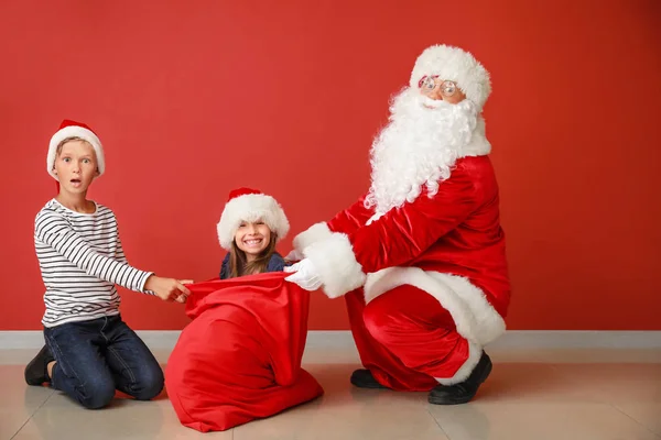 Papá Noel, lindo niño y su hermana pequeña en bolsa cerca de la pared de color — Foto de Stock