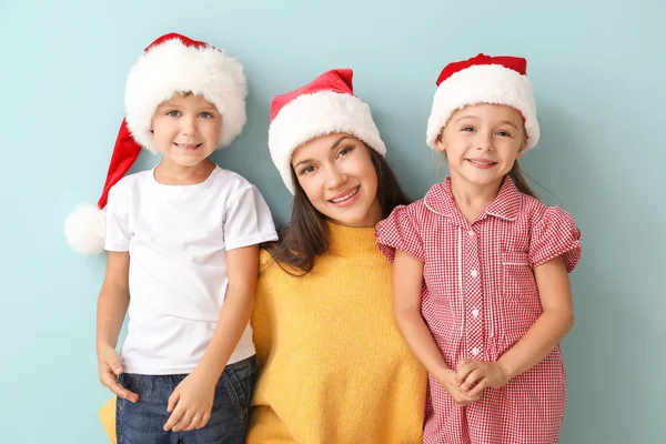Little children and their mother in Santa hats on color background — Stock Photo, Image