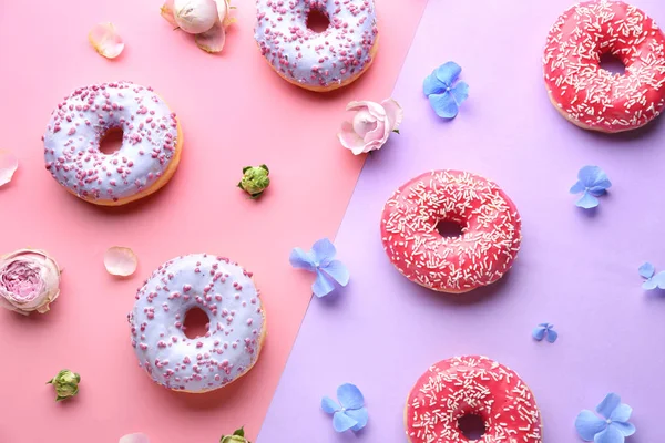 Süße leckere Donuts und Blumen auf farbigem Hintergrund — Stockfoto