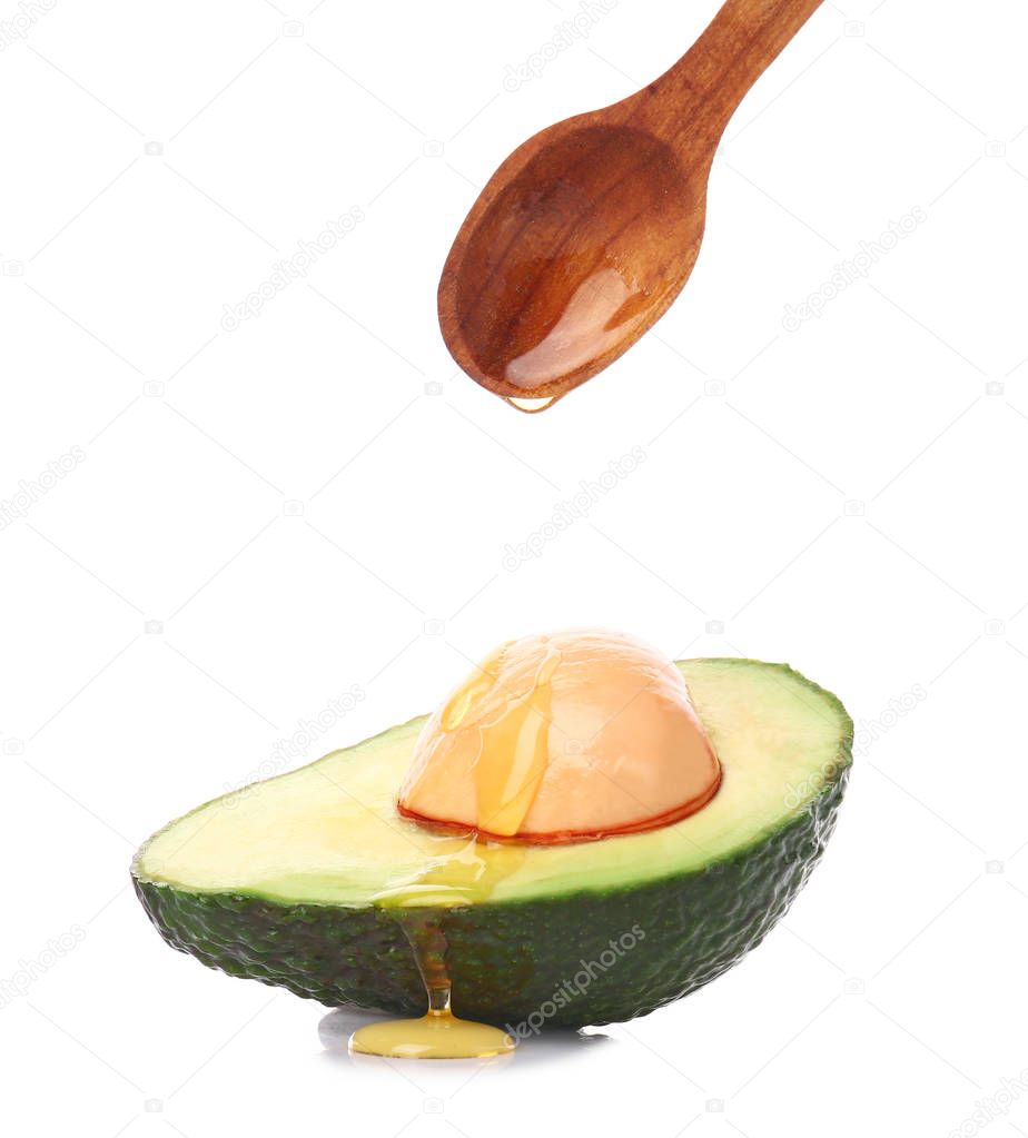 Honey pouring from spoon onto half of avocado against white background