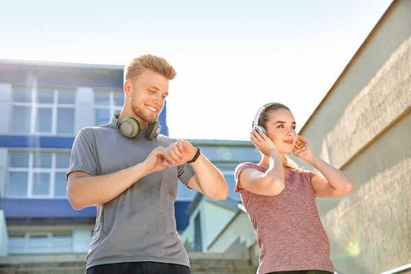 Joven deportivo comprobando el pulso mientras su amigo escucha música al aire libre — Foto de Stock