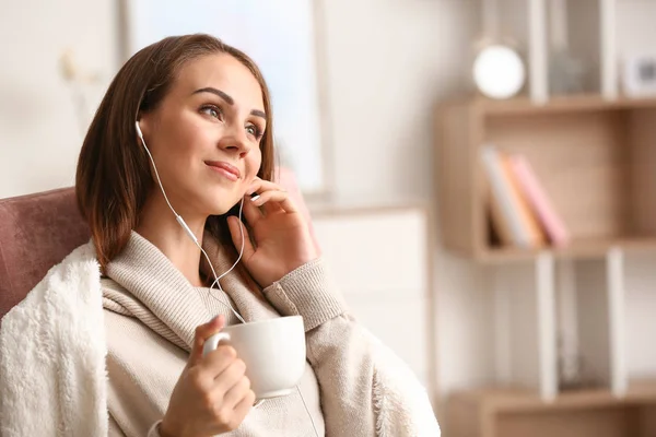 Krásná mladá žena konzumace čaje při poslechu hudby doma — Stock fotografie