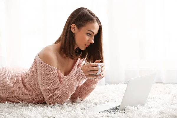 Beautiful young woman with laptop drinking tea at home — Stock Photo, Image