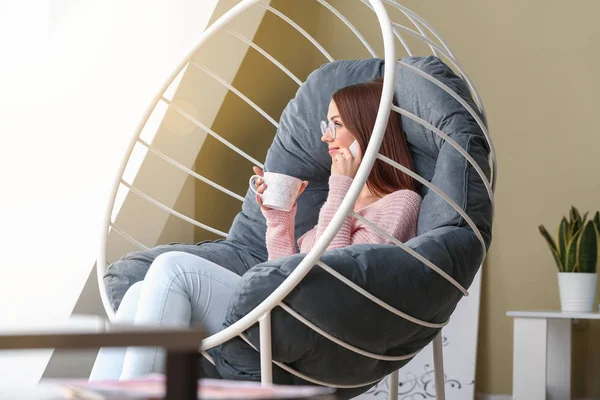 Mooie jonge vrouw drinken thee terwijl praten per telefoon thuis — Stockfoto