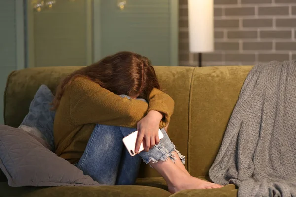Offended teenage girl with mobile phone on sofa at night — Stock Photo, Image