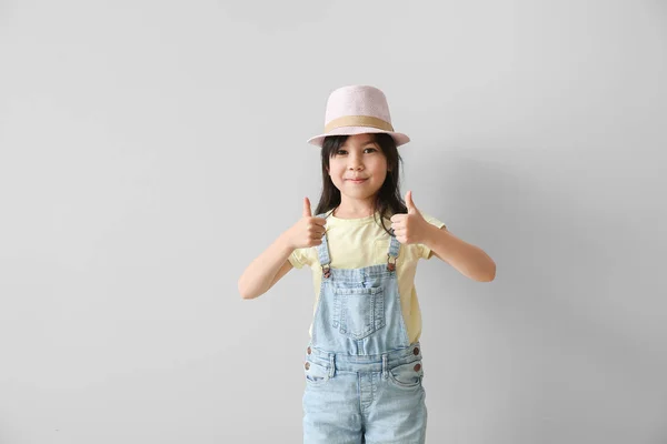 Portrait of stylish little girl showing thumb-up gesture on light background — Stock Photo, Image