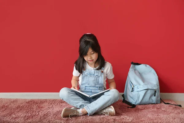 Retrato de colegiala leyendo libro cerca de la pared de color — Foto de Stock