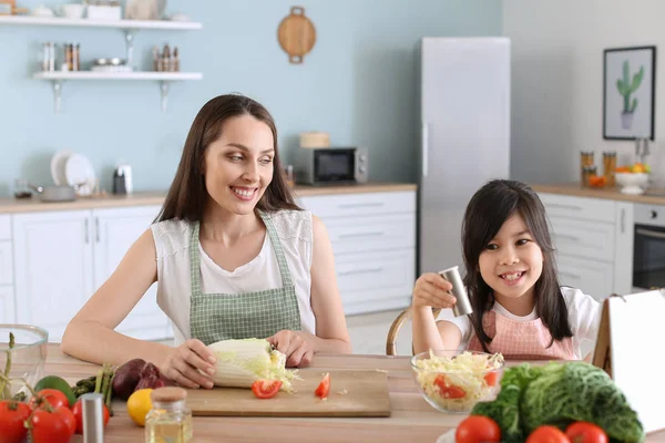 Mãe com filha bonita preparando salada de legumes na cozinha — Fotografia de Stock