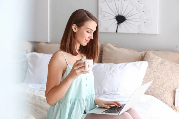 Beautiful young woman with laptop drinking tea at home — Stock Photo, Image