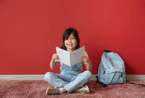 Portrait of little schoolgirl reading book near color wall — Stock Photo, Image