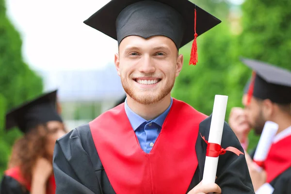 Male student in bachelor robe and with diploma outdoors