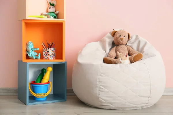 Adorable kitten with teddy bear on beanbag chair in room — Stock Photo, Image