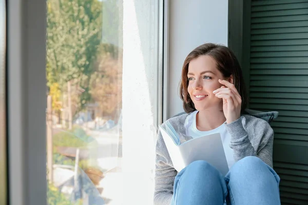 Hermosa joven leyendo libro cerca de la ventana — Foto de Stock