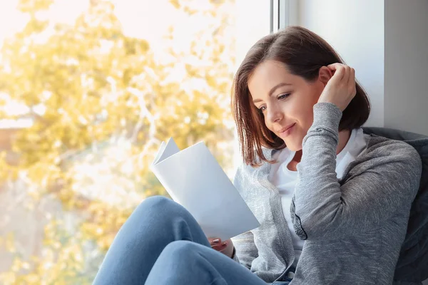 Hermosa joven leyendo libro cerca de la ventana — Foto de Stock