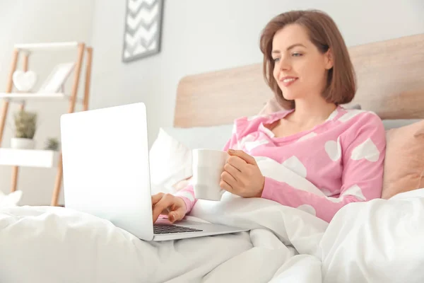 Morning of beautiful young woman with laptop drinking coffee in bed — Stock Photo, Image