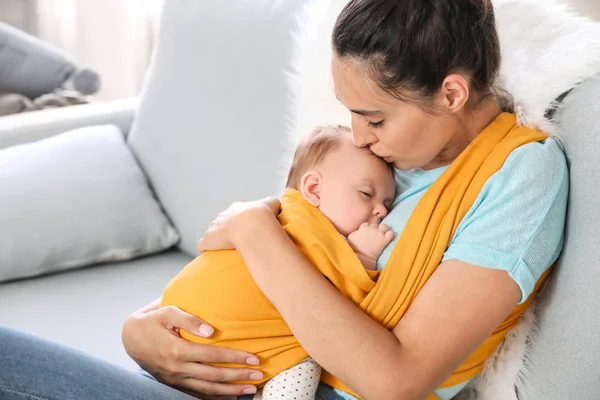 Joven madre con un pequeño bebé en cabestrillo en casa —  Fotos de Stock