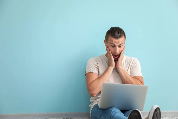 Chockad manliga bloggare med laptop sitter nära färg väggen — Stockfoto
