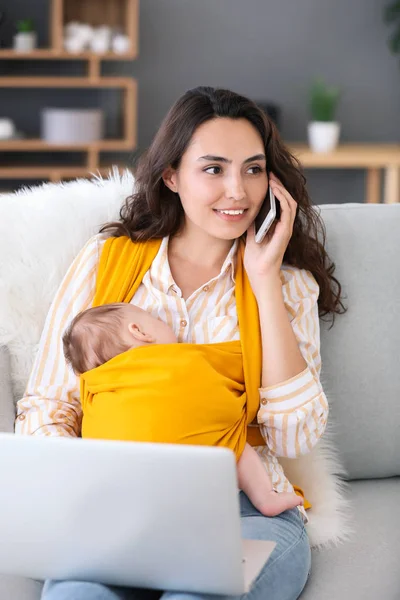 Young mother with little baby in sling working at home — Stock Photo, Image