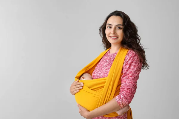 Young mother with little baby in sling on light background — Stock Photo, Image
