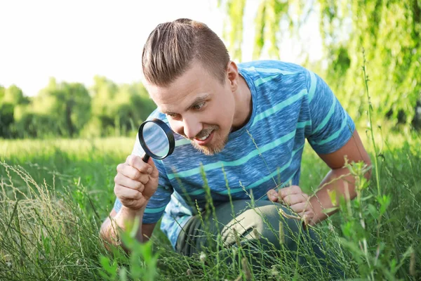 Młody człowiek z lupą studiując naturę na zewnątrz — Zdjęcie stockowe