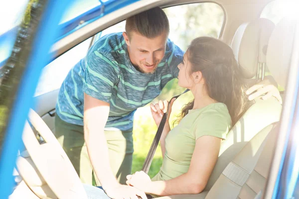 Jonge man helpt zijn vriendin om de auto veiligheidsgordel gesp — Stockfoto