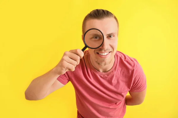 Jonge man met vergrootglas op kleur achtergrond — Stockfoto