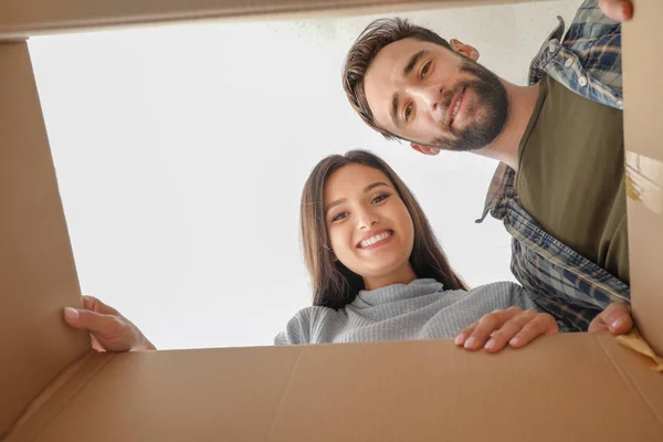 Молодая пара заглядывает в картонную коробку с вещами после переезда в новый дом — стоковое фото
