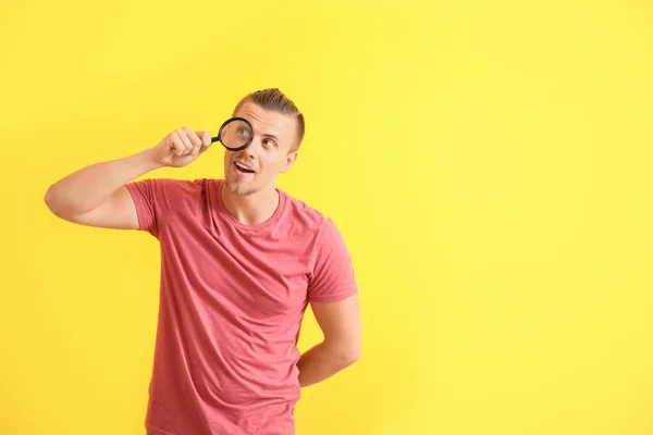 Young man with magnifying glass on color background — Stock Photo, Image