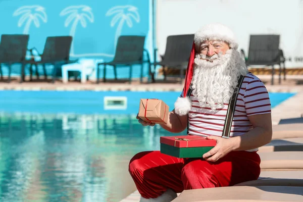 Papai Noel com presentes sentados na beira da piscina — Fotografia de Stock