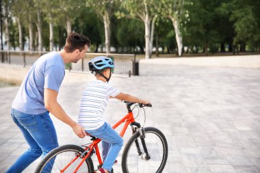 Baba oğluna dışarıda bisiklete binmeyi öğretiyor.