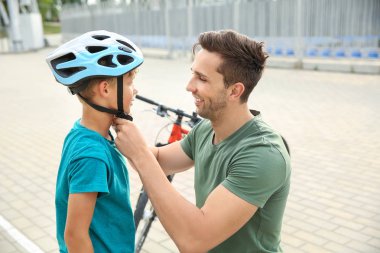 Baba dışarıda bisikletsürmeden önce kask koymak için oğlu yardım