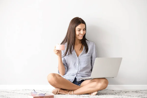 Blogueuse avec ordinateur portable buvant du café tout en étant assise près du mur blanc — Photo