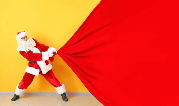 Portrait of Santa Claus pulling big bag against color wall — Stock Photo, Image