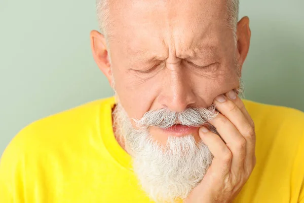 Senior man suffering from toothache against color background, closeup — Stock Photo, Image