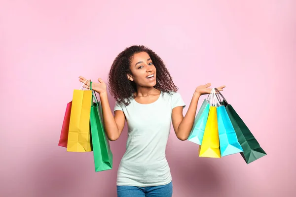 Portrait of happy African-American woman with shopping bags on color background — Stock Photo, Image
