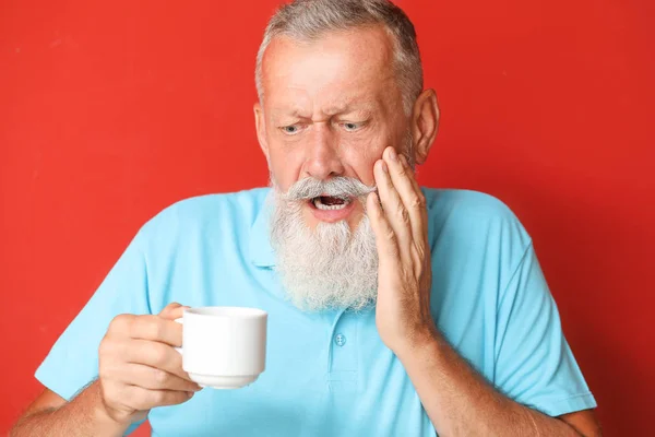 Senior man with sensitive teeth and cup of hot coffee on color background — Stock Photo, Image