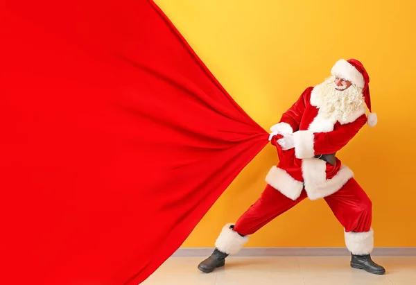 Portrait of Santa Claus pulling big bag against color wall — Stock Photo, Image