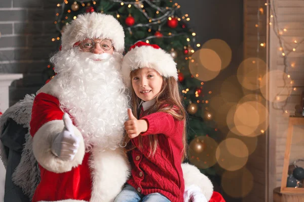 Santa Claus and little girl showing thumb-up in room decorated for Christmas — Stock Photo, Image