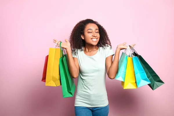 Portrait of happy African-American woman with shopping bags on color background — Stock Photo, Image