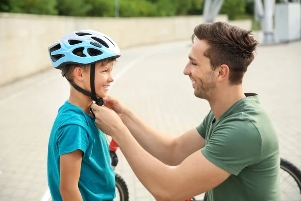 Padre ayudando a su hijo a ponerse el casco antes de montar en bicicleta al aire libre —  Fotos de Stock
