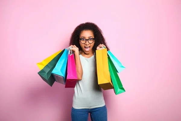 Portrait of excited African-American woman with shopping bags on color background — Stock Photo, Image