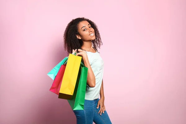 Portrait of happy African-American woman with shopping bags on color background — Stock Photo, Image
