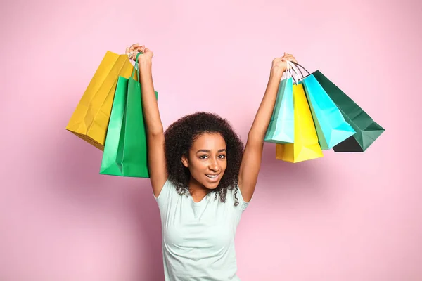 Portrait of happy African-American woman with shopping bags on color background — Stock Photo, Image