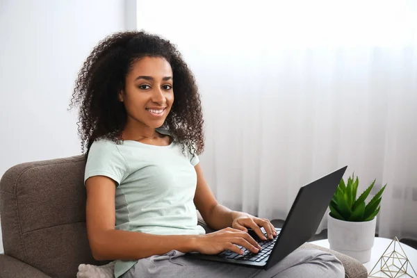 Beautiful African-American woman with laptop sitting in armchair at home — Stock Photo, Image