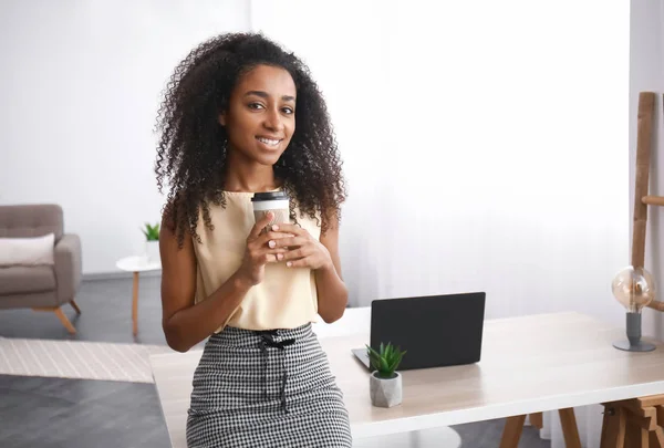 Portrait of beautiful African-American businesswoman with cup of coffee in office — Stock Photo, Image